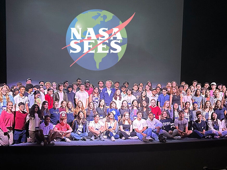 Group photos of 2024 NASA SEES students standing or sitting on a stage with the SEES logo shown on a screen behind them.