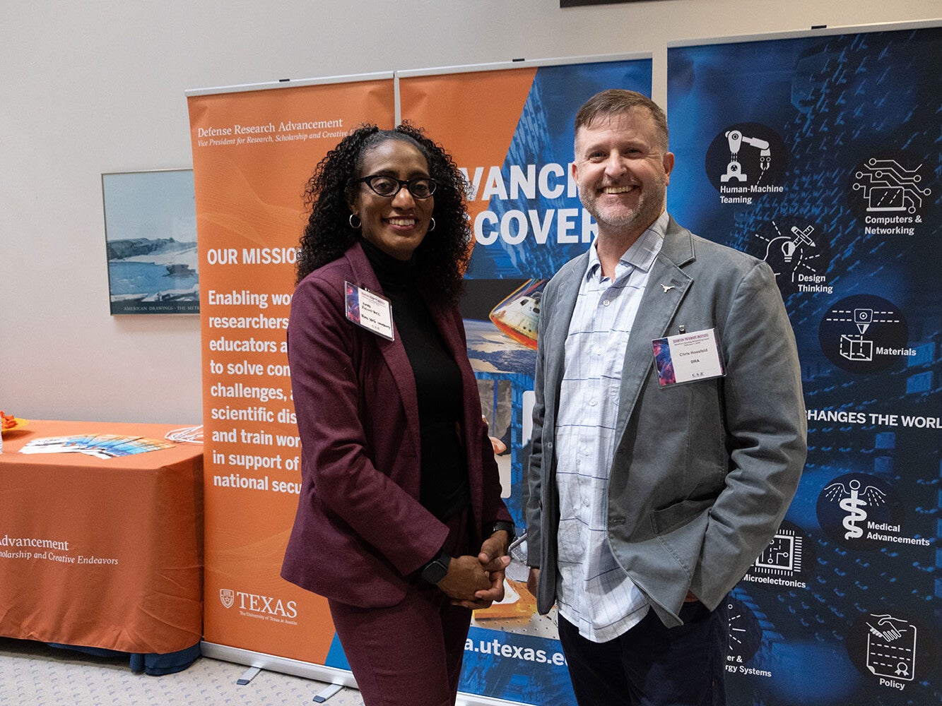 A smiling woman and man standing i front of aorange and yellow pop up banner.
