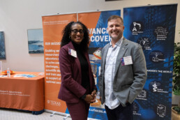 A smiling woman and man standing i front of aorange and yellow pop up banner.