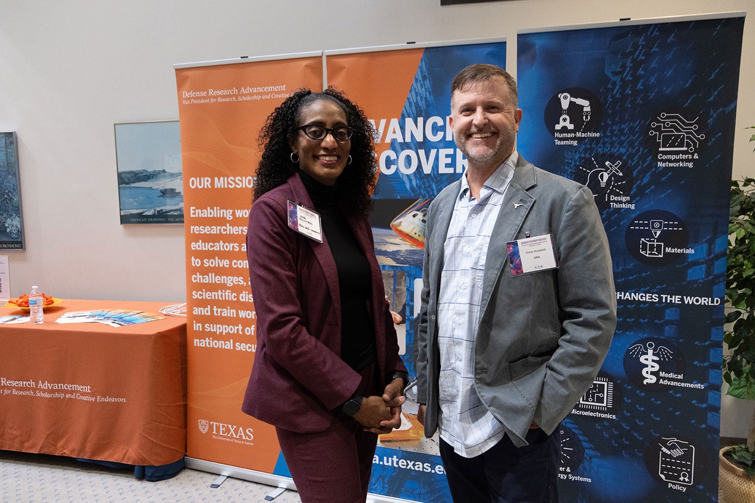 A smiling woman and man standing i front of aorange and yellow pop up banner.