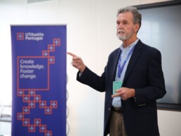 Burke Fort stands in front of banner that says UT Austin Portugal. Create knowledge. FOster change.